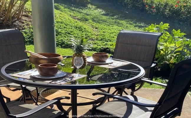 Manualoha 601 lanai dining table set with wooden bowls and a pineapple, overlooking the tropical garden
